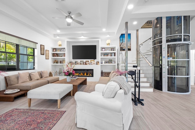 living room featuring light wood-type flooring, a tray ceiling, and ceiling fan