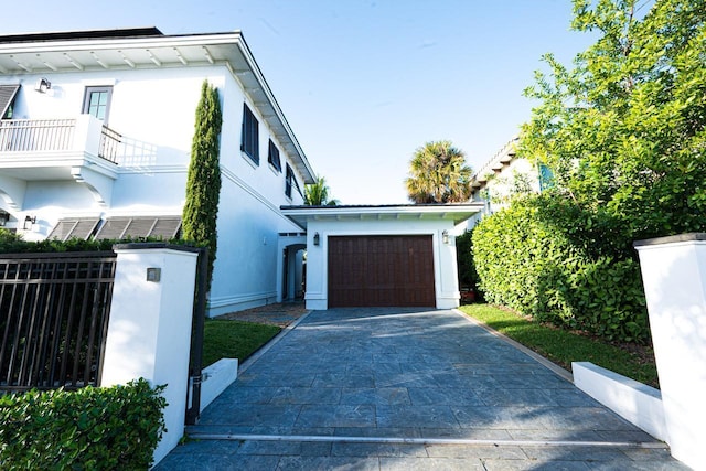 view of home's exterior featuring driveway, a garage, a balcony, fence, and stucco siding