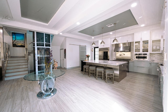 kitchen featuring a kitchen bar, a tray ceiling, exhaust hood, and appliances with stainless steel finishes