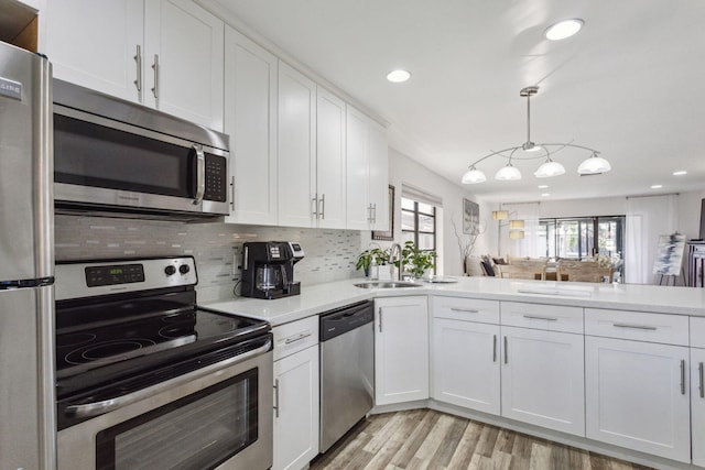 kitchen with white cabinetry, stainless steel appliances, decorative backsplash, sink, and hanging light fixtures