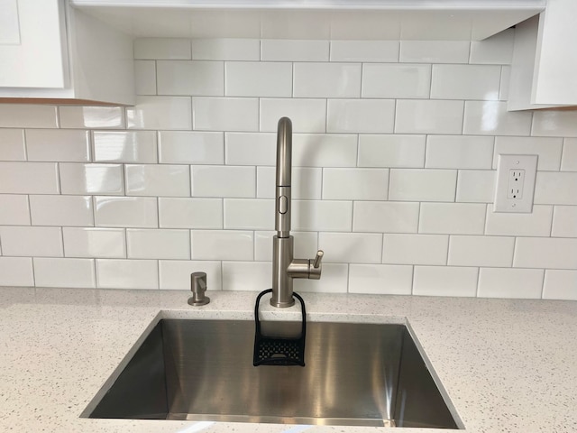 interior details featuring sink, backsplash, white cabinetry, and light stone counters