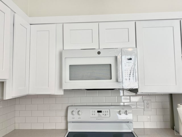 room details featuring decorative backsplash, white cabinetry, and white appliances