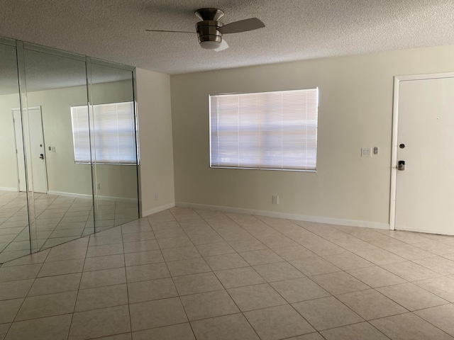 tiled empty room with ceiling fan and a textured ceiling