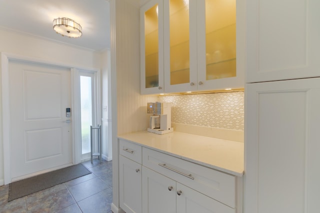 kitchen with light tile patterned floors, backsplash, white cabinetry, and ornamental molding