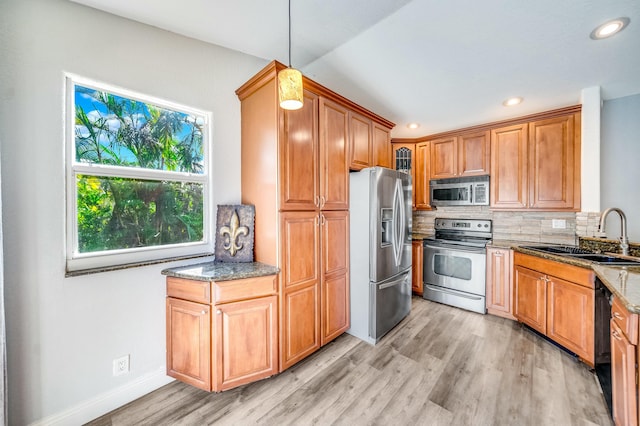 kitchen with appliances with stainless steel finishes, light wood-type flooring, sink, pendant lighting, and dark stone countertops