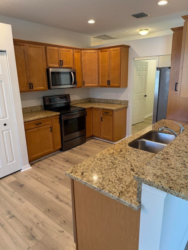 kitchen with sink, light hardwood / wood-style flooring, light stone counters, kitchen peninsula, and stainless steel appliances