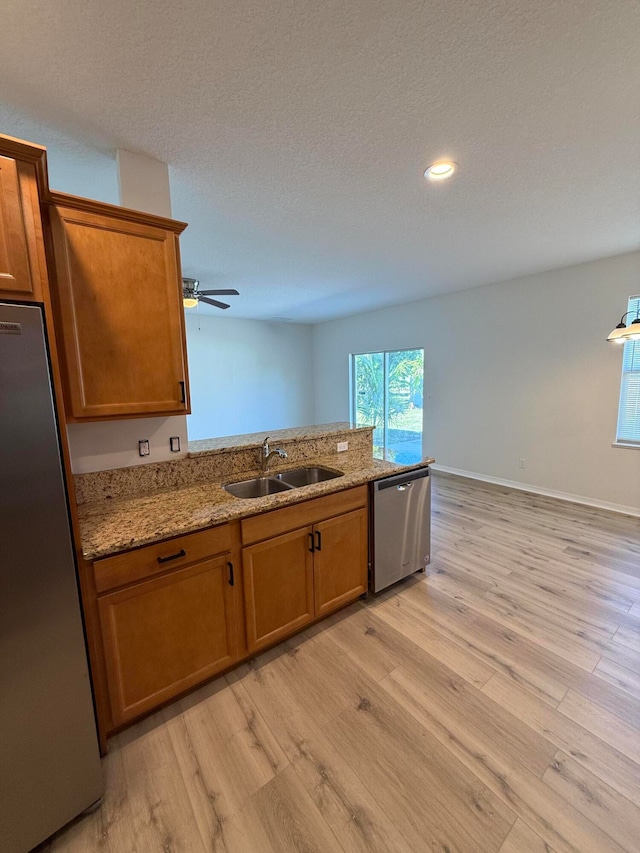 kitchen with light stone countertops, sink, ceiling fan, stainless steel appliances, and light wood-type flooring