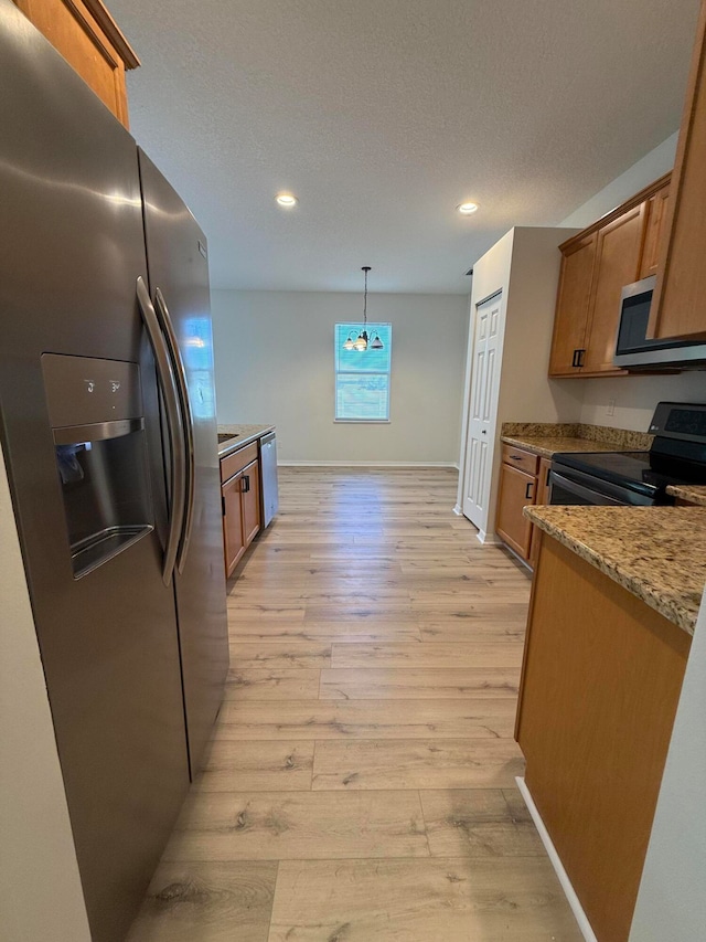 kitchen with pendant lighting, a textured ceiling, appliances with stainless steel finishes, light hardwood / wood-style floors, and light stone counters