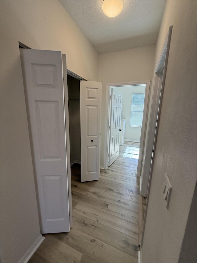 hallway with light hardwood / wood-style floors and a textured ceiling