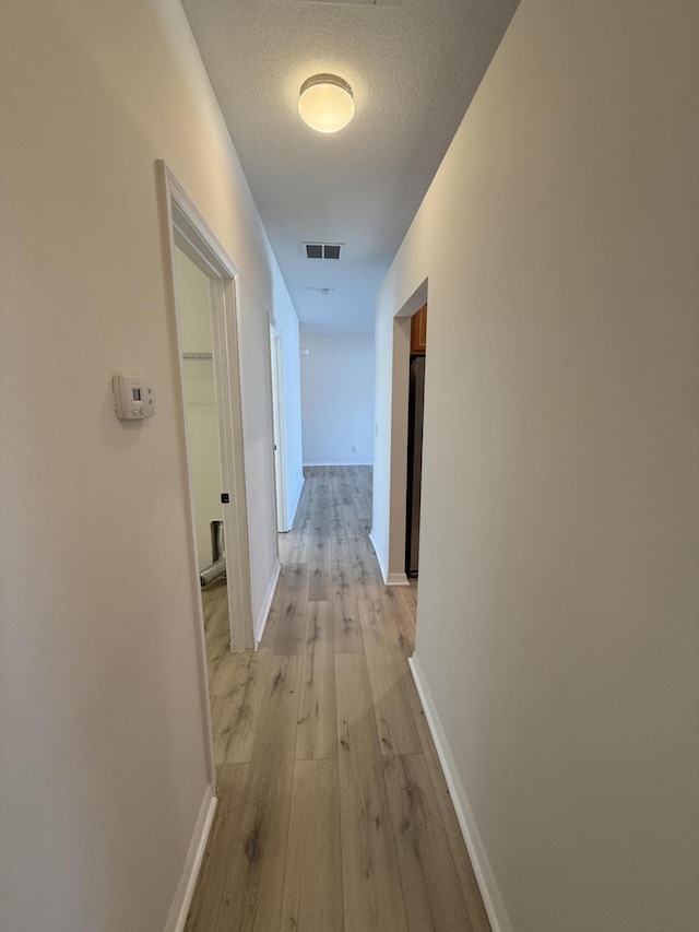 corridor with light hardwood / wood-style flooring and a textured ceiling