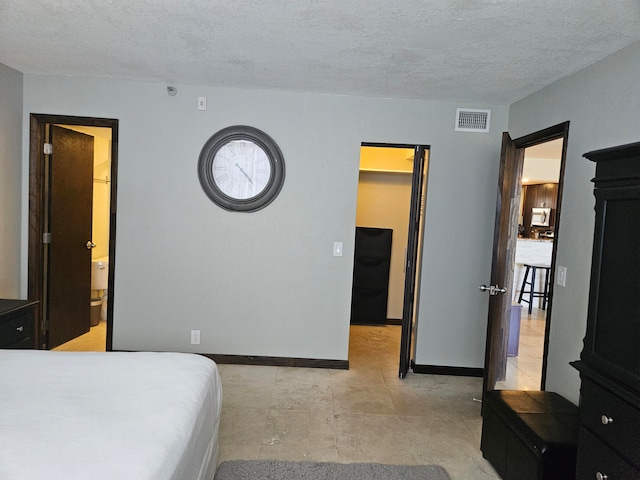 bedroom with a spacious closet, a textured ceiling, and ensuite bath