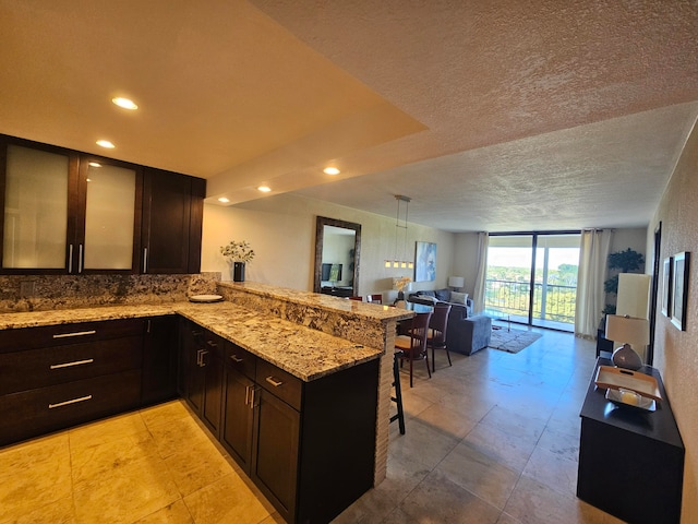 kitchen featuring a kitchen breakfast bar, expansive windows, kitchen peninsula, a textured ceiling, and dark brown cabinets