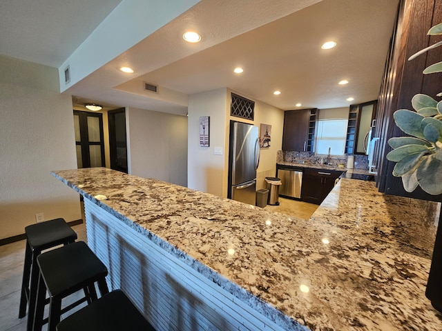 kitchen with kitchen peninsula, light stone countertops, a breakfast bar, and appliances with stainless steel finishes