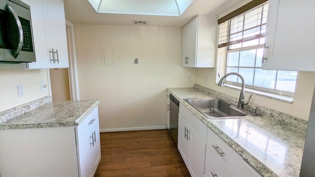 kitchen with a skylight, white cabinetry, sink, stainless steel appliances, and dark hardwood / wood-style flooring