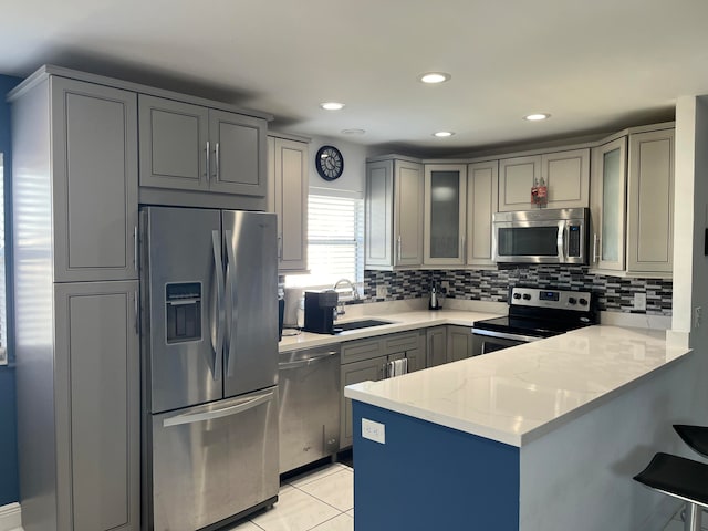 kitchen featuring kitchen peninsula, appliances with stainless steel finishes, backsplash, light stone counters, and sink