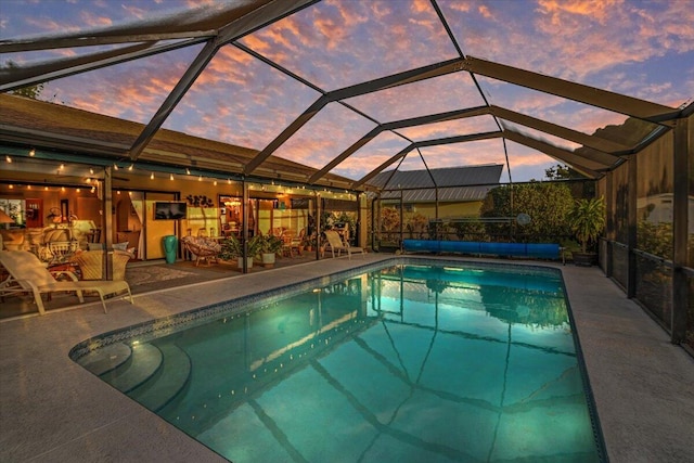 pool at dusk with glass enclosure and a patio