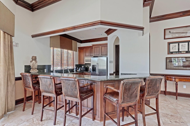 kitchen with kitchen peninsula, stainless steel refrigerator with ice dispenser, crown molding, and a kitchen breakfast bar