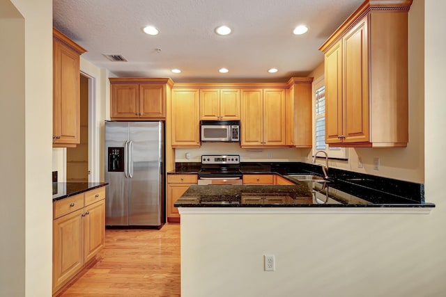 kitchen with kitchen peninsula, appliances with stainless steel finishes, light wood-type flooring, dark stone counters, and sink