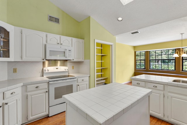 kitchen featuring white appliances, white cabinets, a center island, tile counters, and lofted ceiling