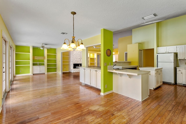 kitchen featuring white cabinets, hanging light fixtures, white fridge, a kitchen bar, and kitchen peninsula