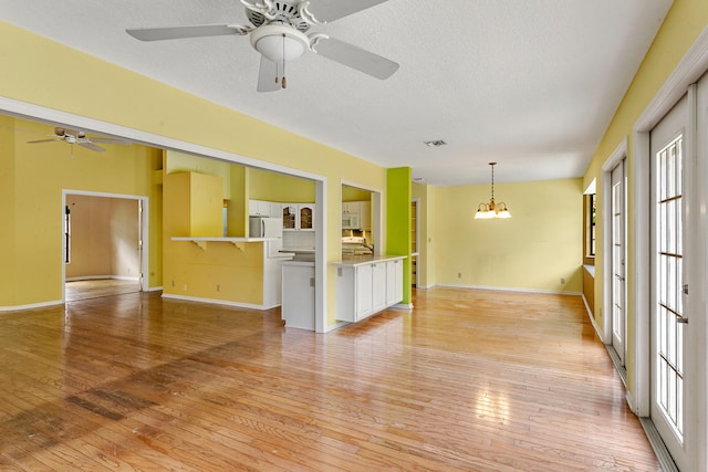 unfurnished living room with ceiling fan with notable chandelier, a textured ceiling, and light wood-type flooring