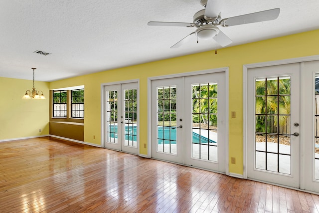 doorway to outside featuring ceiling fan with notable chandelier, light wood-type flooring, a textured ceiling, and french doors