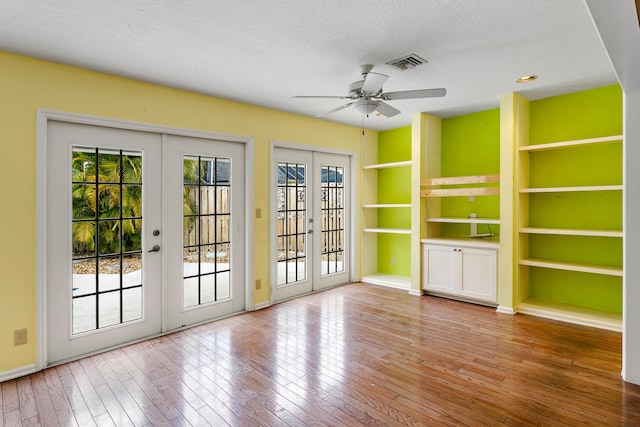 unfurnished living room featuring ceiling fan, light wood-type flooring, a textured ceiling, and french doors