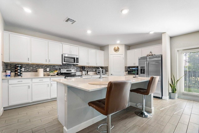 kitchen featuring sink, white cabinets, an island with sink, a breakfast bar, and appliances with stainless steel finishes