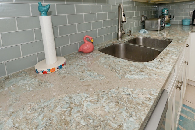 kitchen with decorative backsplash, white cabinets, light stone countertops, and a sink