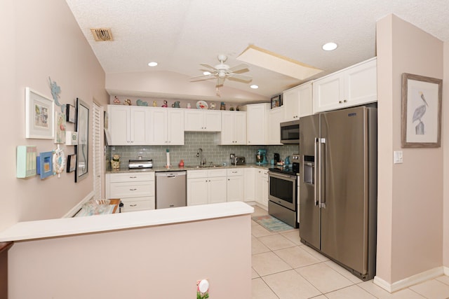 kitchen featuring visible vents, a peninsula, a sink, vaulted ceiling, and appliances with stainless steel finishes