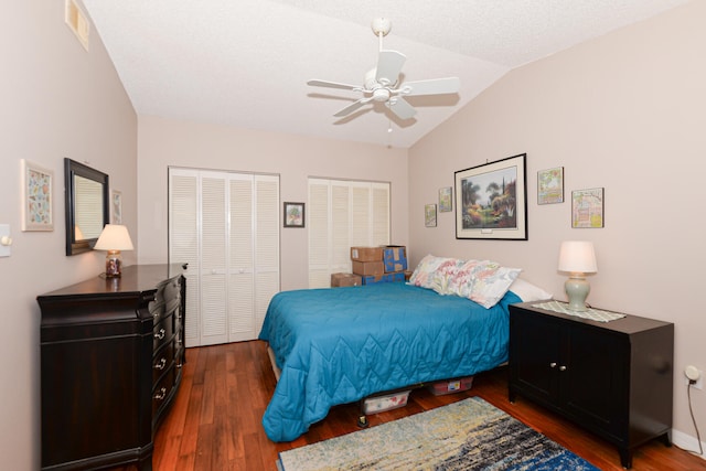 bedroom with ceiling fan, lofted ceiling, two closets, and wood finished floors