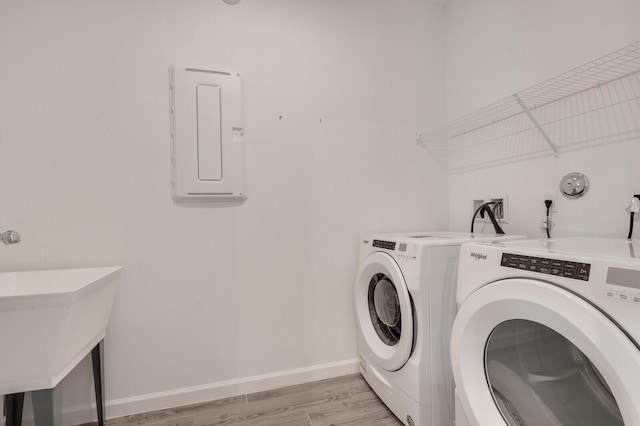 laundry room with sink, electric panel, light hardwood / wood-style flooring, and washing machine and clothes dryer