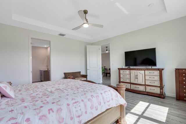 bedroom with ceiling fan, a raised ceiling, connected bathroom, and light hardwood / wood-style flooring