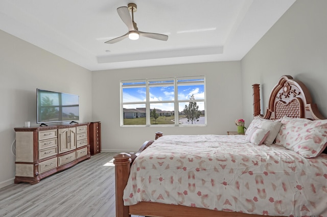 bedroom with ceiling fan, light wood-type flooring, and a tray ceiling