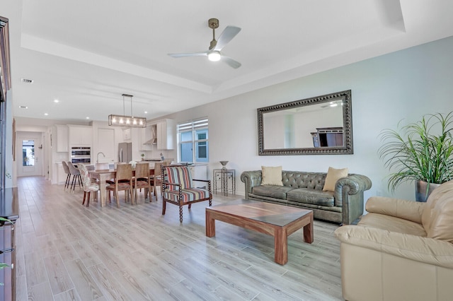 living room featuring ceiling fan, light hardwood / wood-style floors, sink, and a tray ceiling