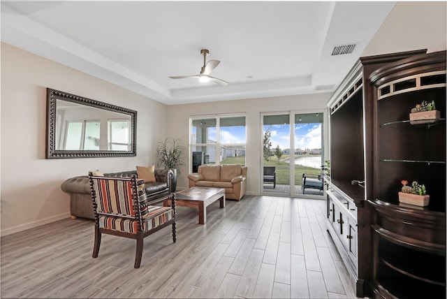 living area with visible vents, light wood-style flooring, a ceiling fan, a tray ceiling, and baseboards