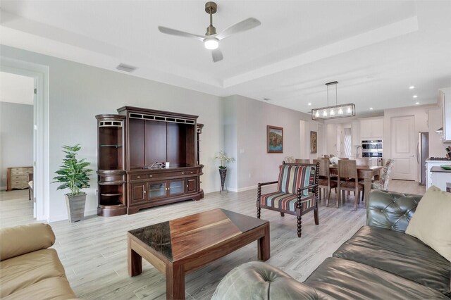 living room with a tray ceiling, ceiling fan, and light hardwood / wood-style flooring