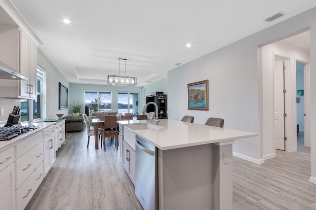 kitchen with a kitchen island with sink, white cabinets, decorative light fixtures, light hardwood / wood-style floors, and stainless steel appliances