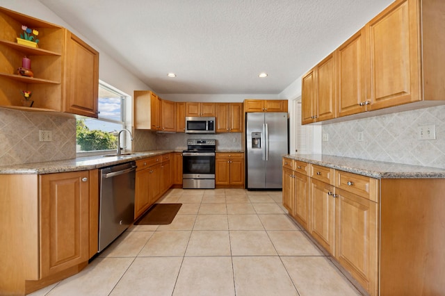 kitchen featuring light stone countertops, sink, backsplash, light tile patterned flooring, and appliances with stainless steel finishes