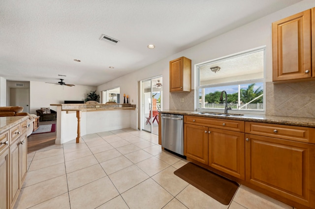 kitchen featuring backsplash, light stone counters, stainless steel dishwasher, ceiling fan, and sink