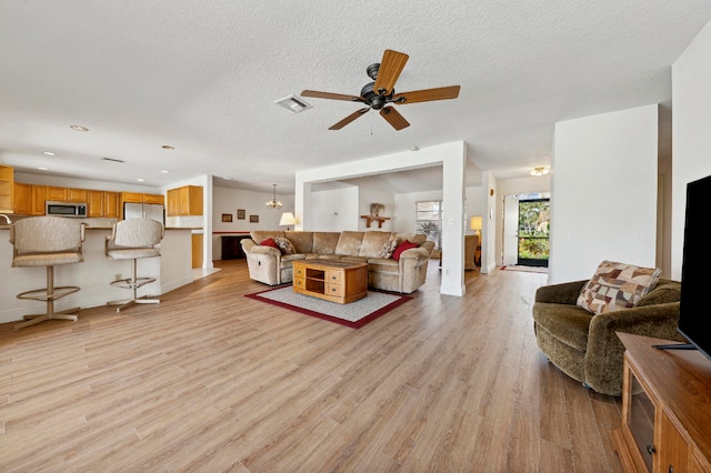 living room featuring a textured ceiling, ceiling fan with notable chandelier, and light hardwood / wood-style floors