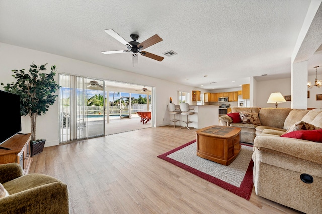 living room featuring a textured ceiling, light hardwood / wood-style flooring, and ceiling fan with notable chandelier