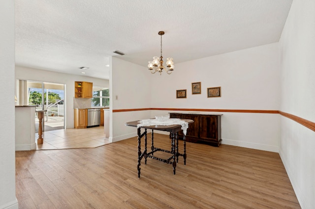 dining space featuring a textured ceiling, light wood-type flooring, and a notable chandelier