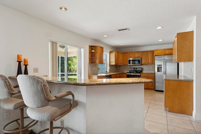 kitchen featuring a breakfast bar area, light tile patterned floors, stone countertops, kitchen peninsula, and stainless steel appliances