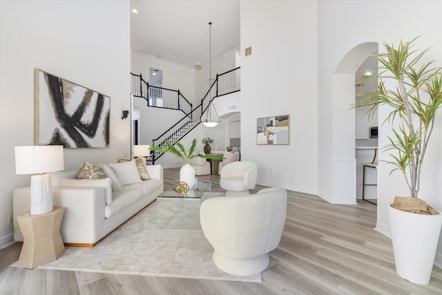 living room with a towering ceiling, ornamental molding, and light wood-type flooring