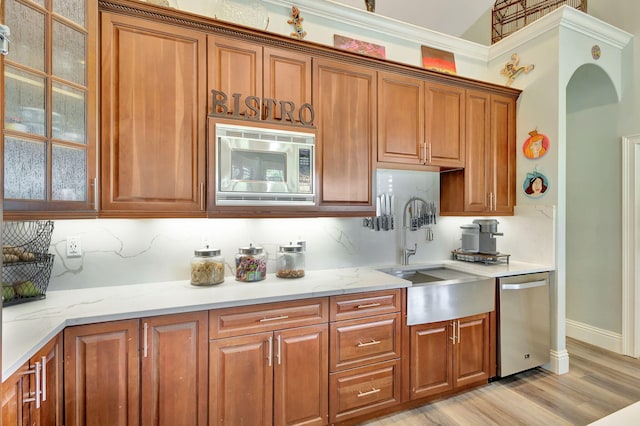 kitchen featuring tasteful backsplash, light stone counters, stainless steel appliances, sink, and light hardwood / wood-style floors