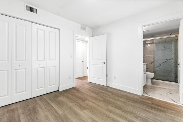 unfurnished bedroom featuring light wood-type flooring, connected bathroom, and a closet