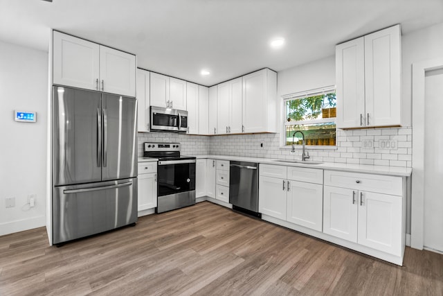 kitchen with decorative backsplash, appliances with stainless steel finishes, sink, white cabinets, and hardwood / wood-style floors