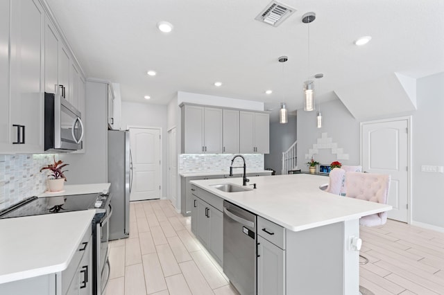 kitchen featuring decorative light fixtures, stainless steel appliances, a center island with sink, and sink