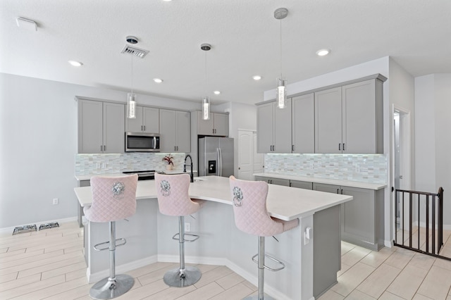 kitchen featuring a kitchen breakfast bar, tasteful backsplash, stainless steel appliances, decorative light fixtures, and an island with sink